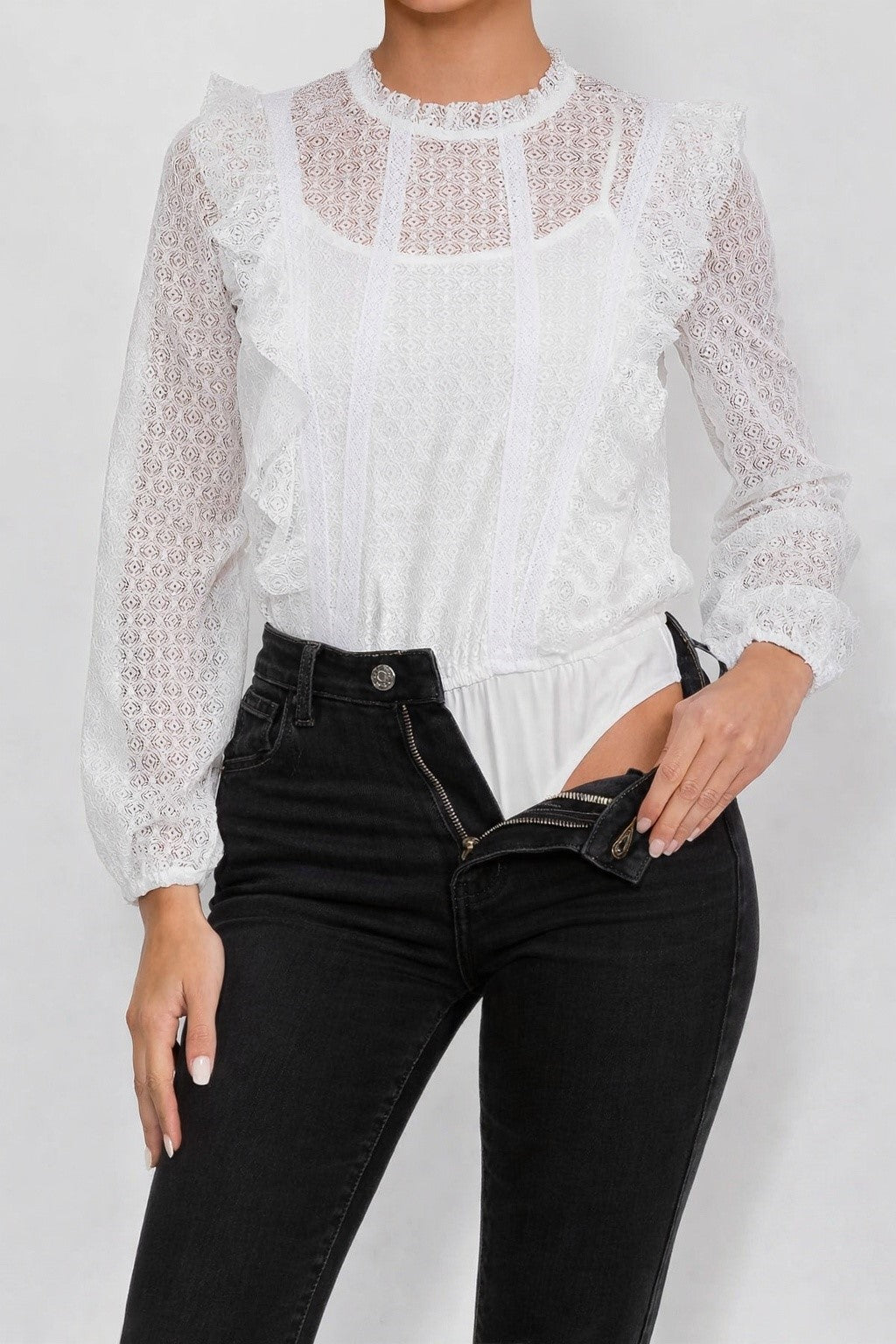 Close up view of a woman wearing the Opaline Ruffle Bodysuit white lace blouse and black pants on a plain background