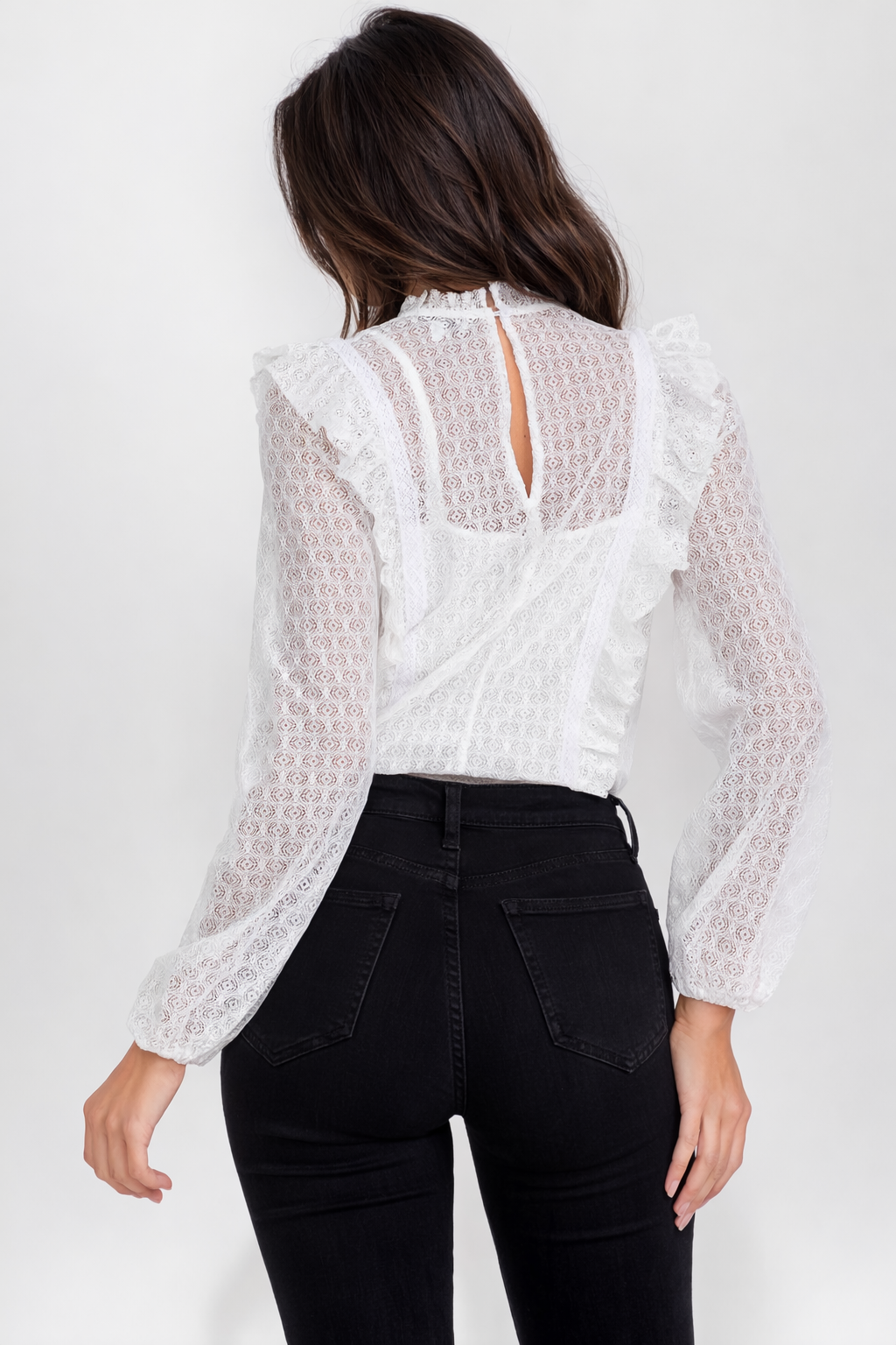 Back view of a woman wearing the Opaline Ruffle Bodysuit white lace top and black pants on a white background